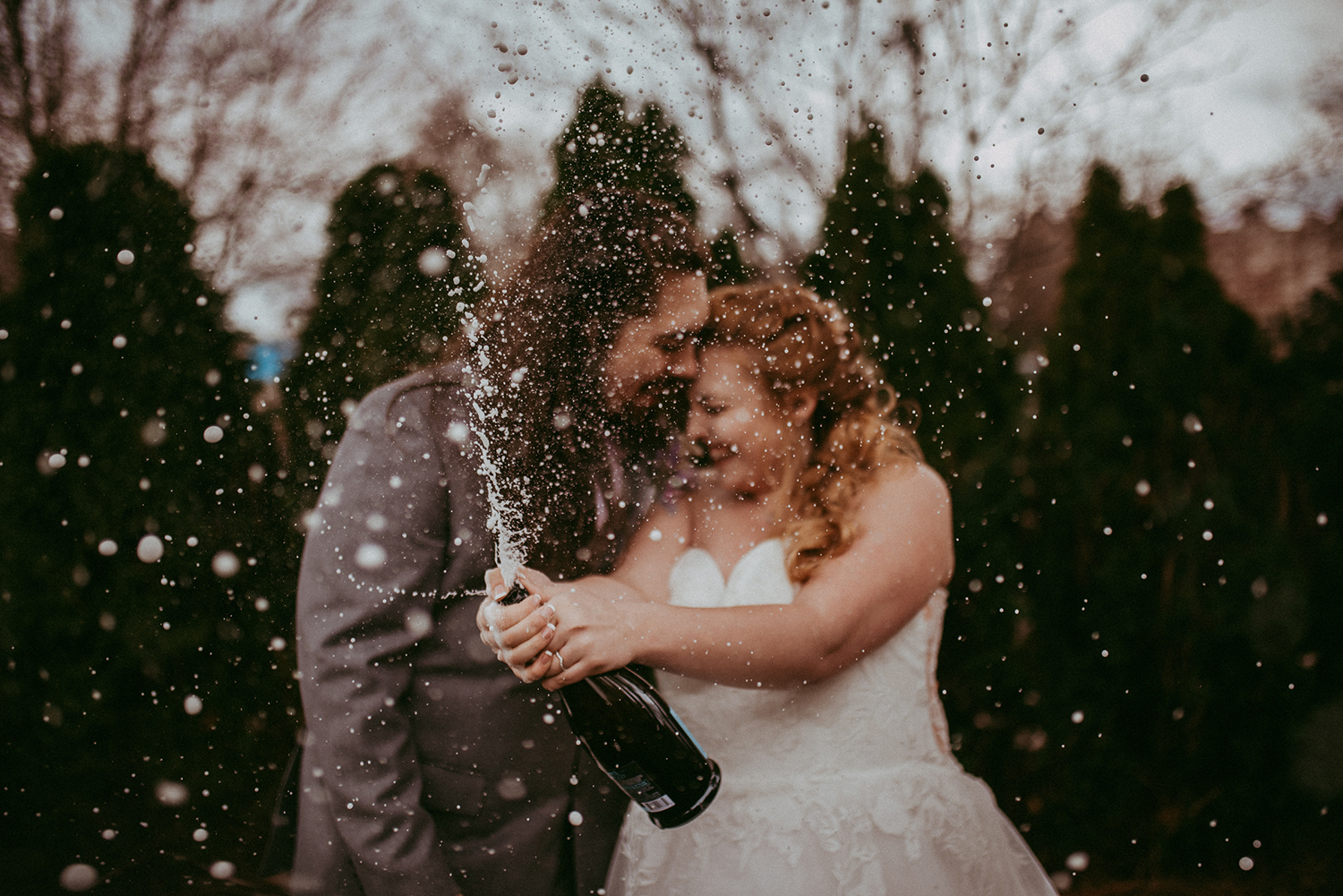 Couple pressing their foreheads together as a champagne bottle sprays between them