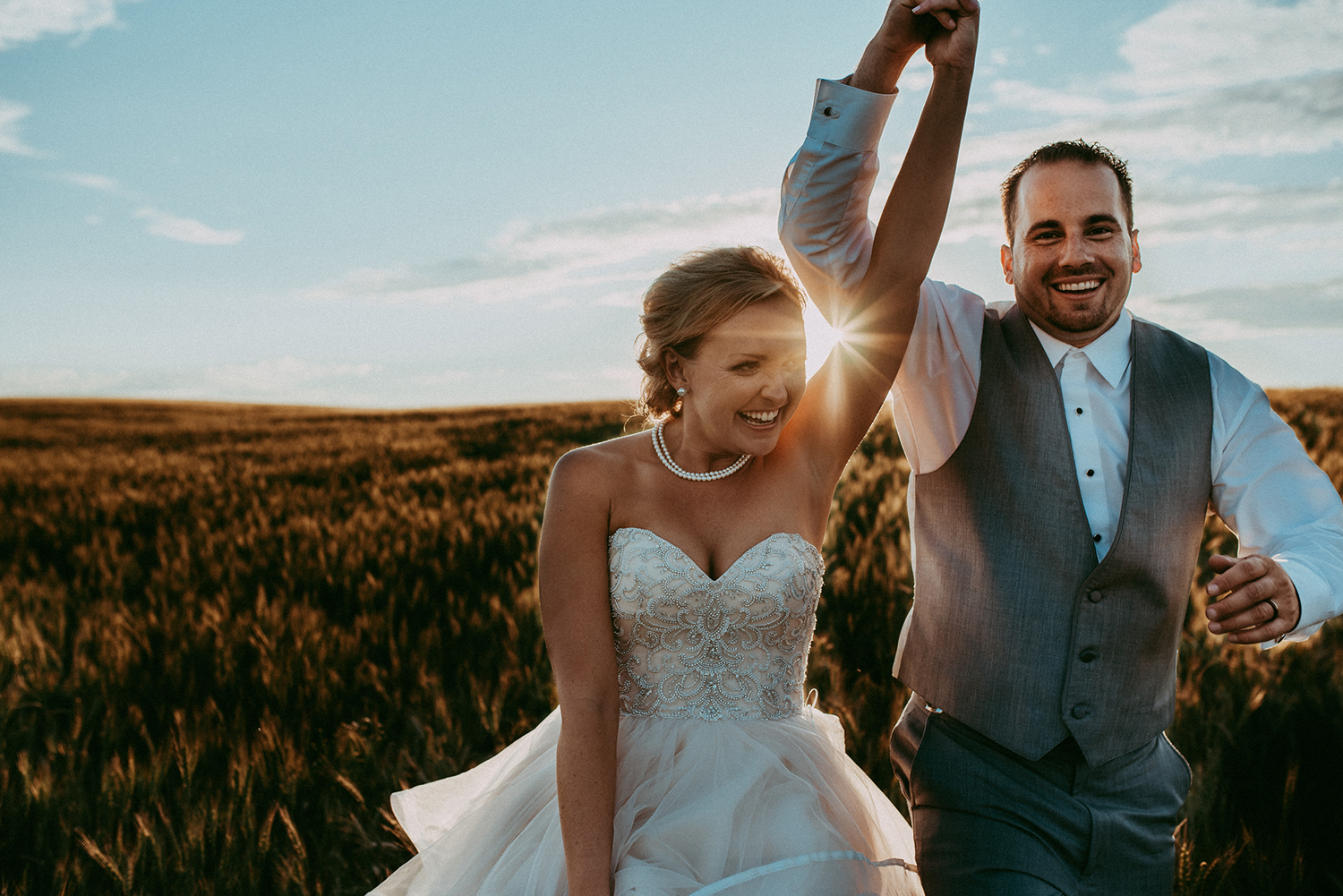 Bride and groom laughing as they twirl through a wheat field at sunset