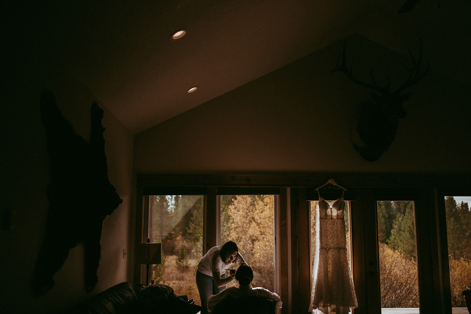 Dim cabin interior with a wedding dress hanging in the window and a couple embracing in silhouette